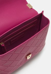 Öppen kviltad lila läderhandväska med guldfäste, som visar texturerat innerväskfack och sömnadsdetaljer.