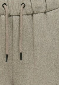 Helle graue Hose aus strukturiertem Stoff, mit einem Kordelzugverschluss aus beigen Schnüren und schwarzen Metallspitzen.