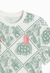 T-shirt bianca con motivo geometrico verde, con logo Puma rosso ed emblema circolare dell'AC Milan in rosso e bianco.