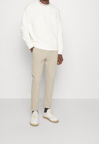 Vit crewneck-tröja med en krage med svarta ränder, ihop med ljusbeige chinos och vita sneakers med guldsål.