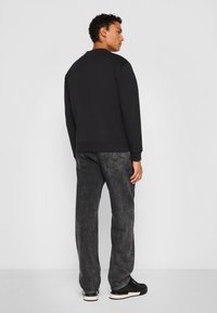 Black sweatshirt with a crew neckline, paired with dark gray jeans. The outfit features a relaxed fit and textured fabric.