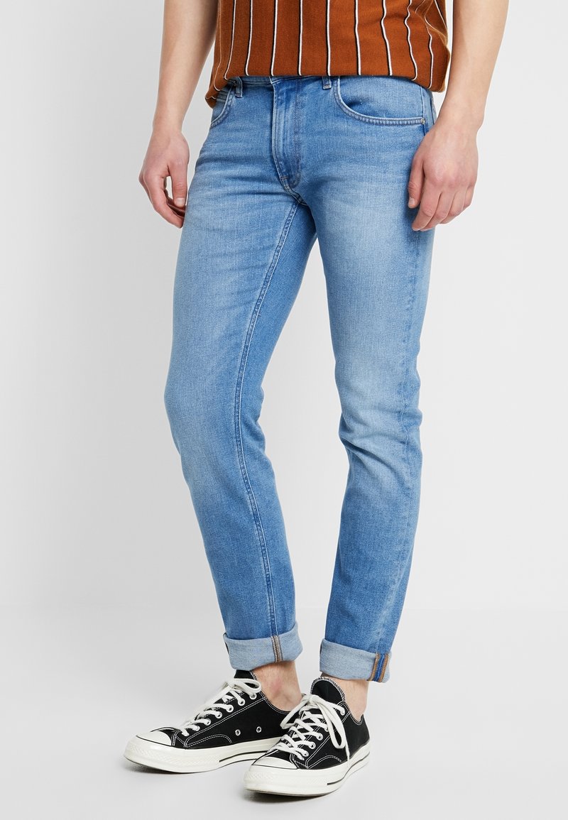Ljust blå denimjeans med slim fit, rullade mudd och subtila blekningar. Matchat med svarta kanvas sneakers med vita snörning.