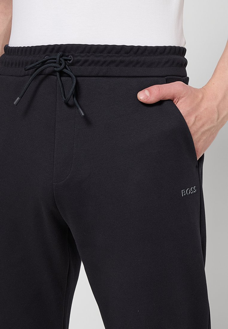 Pantaloni sportivi neri con vita elastica e coulisse regolabile; presenta una tasca laterale e un logo in rilievo discreto. Tessuto morbido e strutturato.