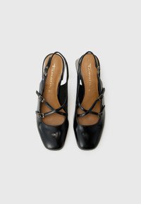 Schwarze Leder-Slingback-Schuhe mit quadratischen Zehen, ausgestattet mit einem Querstegdesign und verstellbaren Schnallen. Hellbraune Einlegesohlen sind sichtbar.