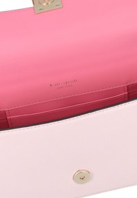 Pink leather handbag interior with a smooth texture, featuring a contrasting inner lining and a gold logo. Magnetic closure on the flap.
