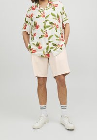 Chemise à manches courtes, boutonnée, avec un motif floral en blanc, rose et vert. Associée à un short rose pâle et des baskets blanches.