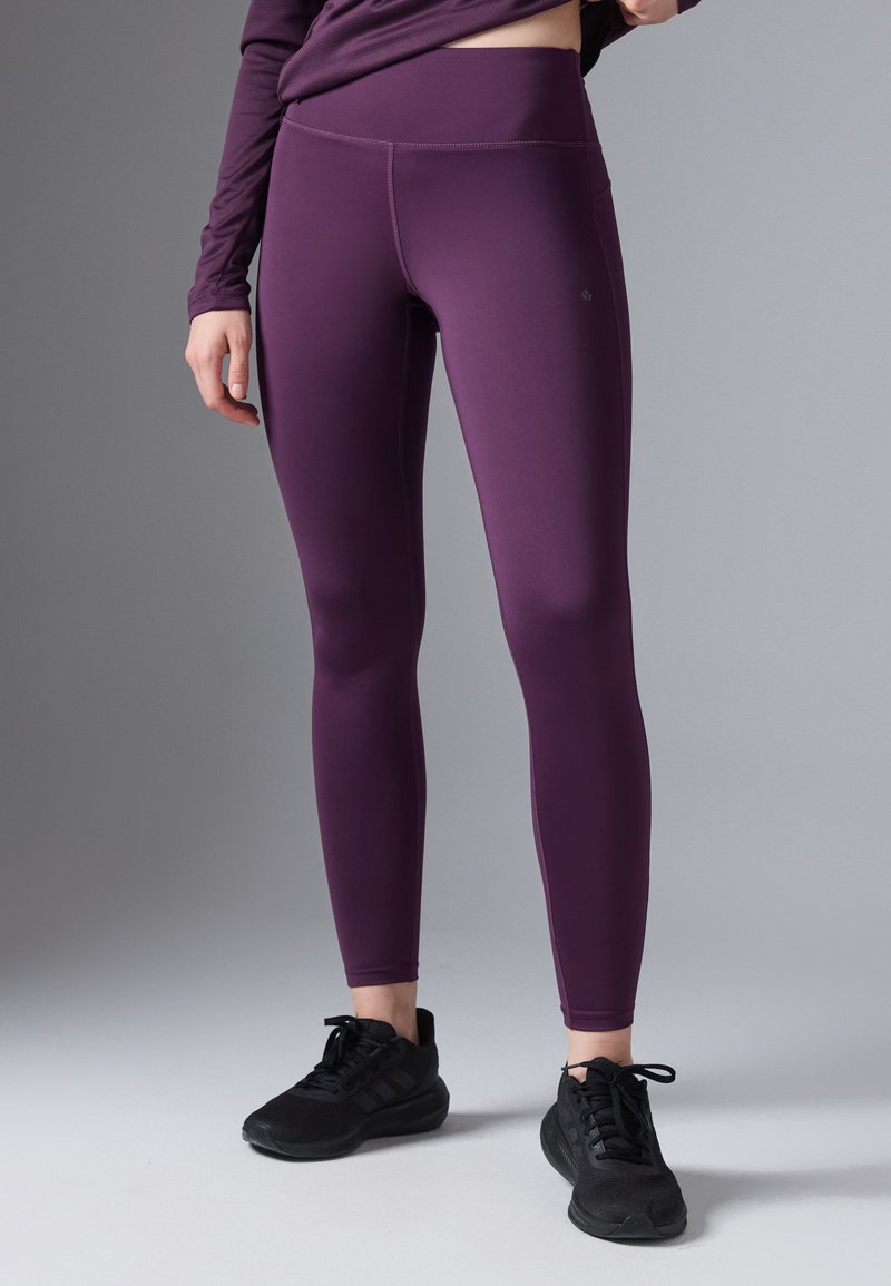 Leggings morados hechos de un material elástico, con una cinturilla alta, textura suave y costuras planas, combinados con zapatillas deportivas negras.