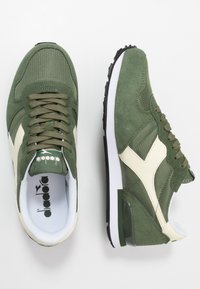 Green suede sneakers with mesh and leather accents, featuring beige logo detail, textured laces, and a white midsole with black tread.