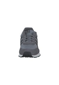 Zapatilla deportiva gris que presenta una combinación de materiales de ante y malla, tres franjas negras y una suela de goma con una media suela blanca.