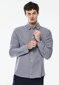 Pruhovaná košile s knoflíky v modro-bílé barvě vyrobená z bavlny. Dlouhé rukávy, standardní límec a přední knoflíky. Rovný lem s manžetami.