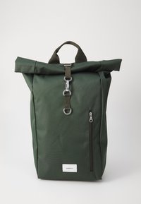Sac à dos vert à rabat en tissu durable, avec une poche frontale zippée et des accents en métal. Design simple et fonctionnel.
