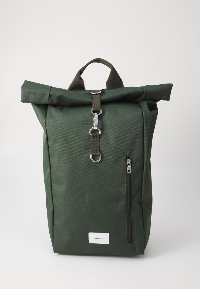 Sac à dos vert à rabat en tissu durable, avec une poche frontale zippée et des accents en métal. Design simple et fonctionnel.