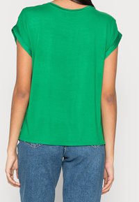 T-shirt vert à manches courtes en tissu léger ; encolure arrondie ; coupe décontractée ; texture subtile ; porté avec un jean bleu taille haute.