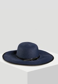 Szeroka, granatowa słomkowa czapka z czarnym paskiem i szczegółem w postaci klamry. Teksturowana powierzchnia, okrągły kształt i kontrastowy design krawędzi.