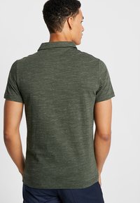 Dark green short-sleeve polo shirt made of textured fabric, featuring a classic collar and a relaxed fit, visible stitching details on the back.