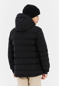 Schwarze Steppjacke mit Kapuze, ausgestattet mit horizontalem Steppmuster, elastischen Bündchen und glatter Textur. Trägt eine schwarze Strickmütze.