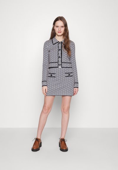 Rochie cu model alb-negru, cu guler, mâneci lungi și butoniere pe față. Are două buzunare în față și margini contrastante. Pantofi maro.