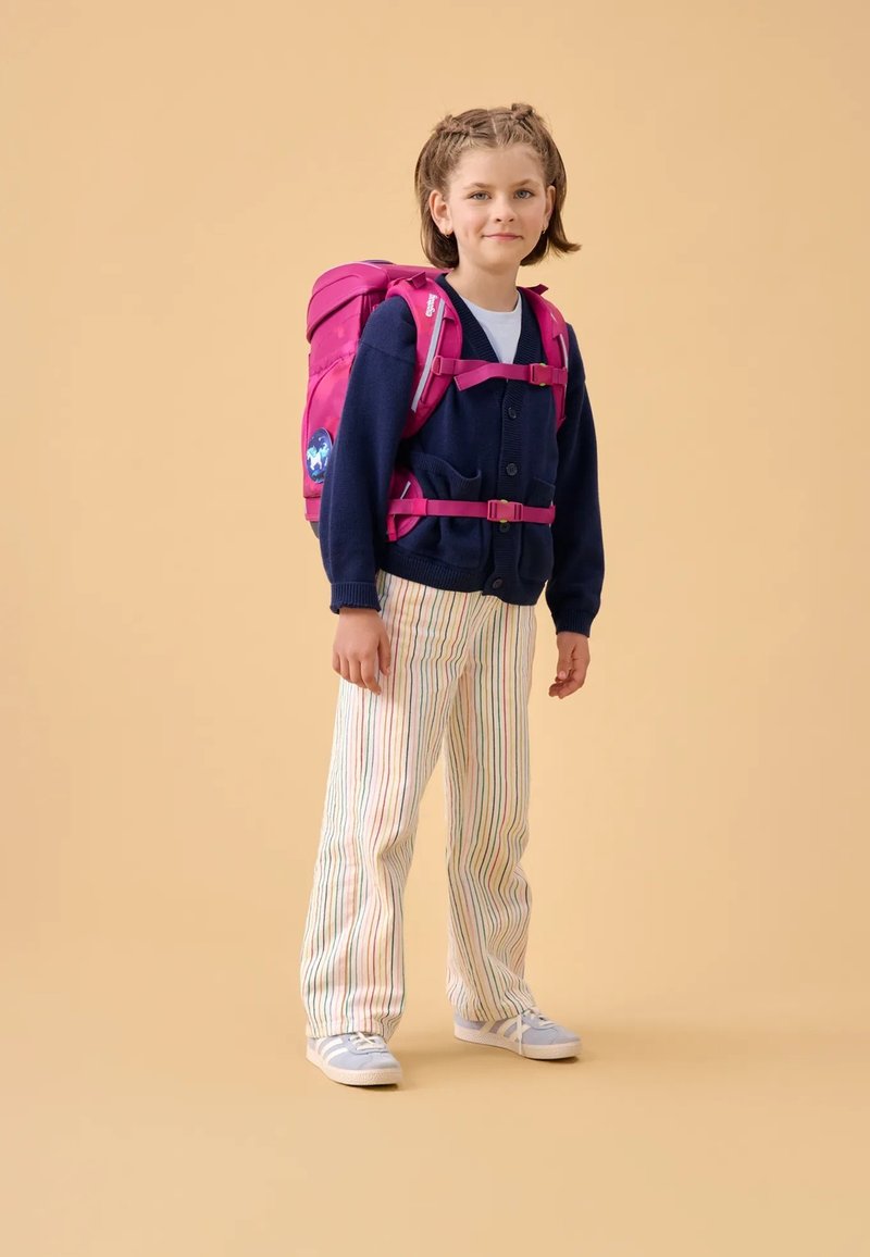 Roze rugzak met verstelbare schouderbanden, gedragen over een marineblauwe cardigan, witte blouse en gestreepte broek. Bevat een cirkelvormige graphic.