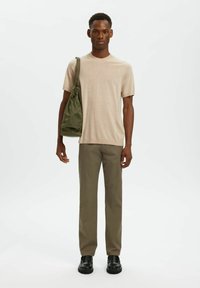 Chemise en tricot beige à manches courtes, pantalon vert olive et chaussures noires ; portant un sac à cordon vert. Design simple et moderne.