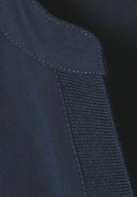 Close-up van donkerblauwe stof met gestikte naad en een verticale strook van textuurklittenband (Velcro).