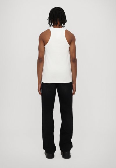 Hvid tanktop med en tætsiddende design, som har brede ærmeåbninger, parret med sorte lige ben jeans og kraftige sorte sko.