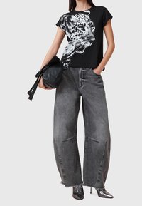 T-shirt en coton noir avec un graphisme de léopard blanc, associé à un jean gris taille haute et ample, dotés de découpes uniques et d'ourlets effilochés.