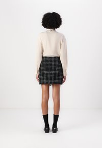 Beige long-sleeve blouse paired with a black and white checked mini skirt. The skirt features a fringe hem and is worn with black socks and shoes.