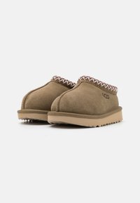 Bruna mockaskor med slip-on-design och en texturerad yttersula. Har en flätad kant längs kragen och en logotyp på sidan.