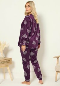 Lila samettinen yöpuku, jossa on valkoisia sydänkuvioita, pitkät hihat ja joustavat hihnat housuissa. Yksinkertainen, rento leikkaus.