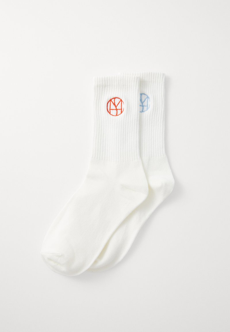 Calcetines de algodón blanco con puños acanalados, que presentan logotipos circulares en rojo y azul en cada calcetín. Textura suave y diseño de longitud media.