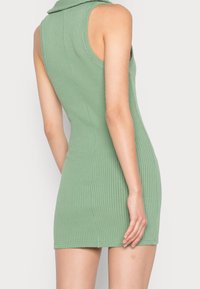 Zelené žebrované šaty bez rukávů s límečkem, přiléhavým střihem a hladkou texturou, končící nad polovinou stehna.