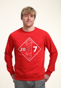 Felpa rossa con grafica a diamante contenente i numeri "20" e "7", e un'illustrazione di skateboard in bianco. Maniche lunghe e scollo rotondo.