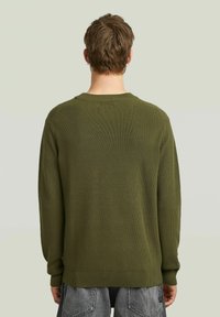 Pull en tricot vert avec une texture côtelée, col rond classique et manches longues. Coupe légèrement oversize avec des poignets et un ourlet côtelés.
