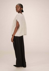 Pull en gris clair, moelleux et à manches courtes, associé à un pantalon noir à jambes larges. La texture semble douce et confortable.