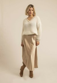 Pull blanc en maille à col en V avec des manches longues, associé à une jupe en satin beige et des bottines en cuir suédé tan.
