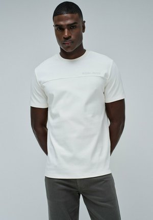 Camiseta blanca de manga corta con cuello redondo, que presenta un panel texturizado en el pecho y el logo "Salsa Jeans" en gris claro.