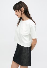 Biała krótka koszulka z bawełny z okrągłym dekoltem, krótkimi rękawami i teksturowanym logo. Połączona z ciemną spódnicą jeansową z kieszeniami.