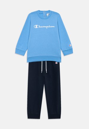 Blå sweatshirt med vitt "Champion"-logotyp, i kombination med marinblå träningsoverallsbyxor med justerbar dragsko och logotypdetaljer på ärmarna.