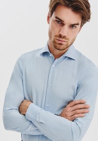 Jasnoniebieska koszula z długim rękawem, wykonana z gładkiego materiału. Posiada kołnierzyk zapinany na guziki oraz guziki z przodu. Prosty design bez wzorów.