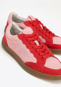 Sneaker in suede con una combinazione di colori rosa e rosso, pannelli testurizzati, dettagli ondulati e lacci rossi su una suola in gomma beige.