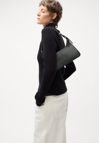 Sac à main en cuir noir avec un design structuré, doté d'une seule bandoulière et d'une texture lisse. Présenté sur un fond neutre.