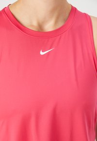 Ružičasti sportski top s okruglim izrezom i bijelim Nike logotipom na prsima. Glatka tkanina s prilagođenim dizajnom i bez istaknutih uzoraka.
