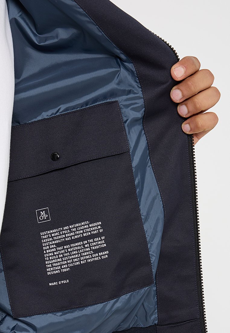Marineblaues Zip-Up-Jackett mit einem glatten, glänzenden Innenfutter. Verfügt über eine rechteckige Tasche mit bedrucktem Text und einem Druckknopfverschluss.