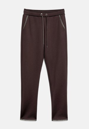 Pantalon de survêtement marron foncé avec taille à cordon, poches avant et bordure argentée sur les contours des poches et les poignets de jambes.