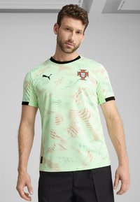 Svetlo zelena športna majica z pikčasto zasnovo, ki vsebuje črne poudarke, okroglo ovratnik in logotip portugalske nogometne reprezentance na prsih.