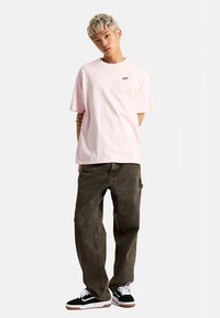 Jasnoróżowa bawełniana koszulka z okrągłym dekoltem, krótkimi rękawami i małym logo; w zestawieniu z ciemnozielonymi, oversize'owymi dżinsami oraz czarnymi tenisówkami.