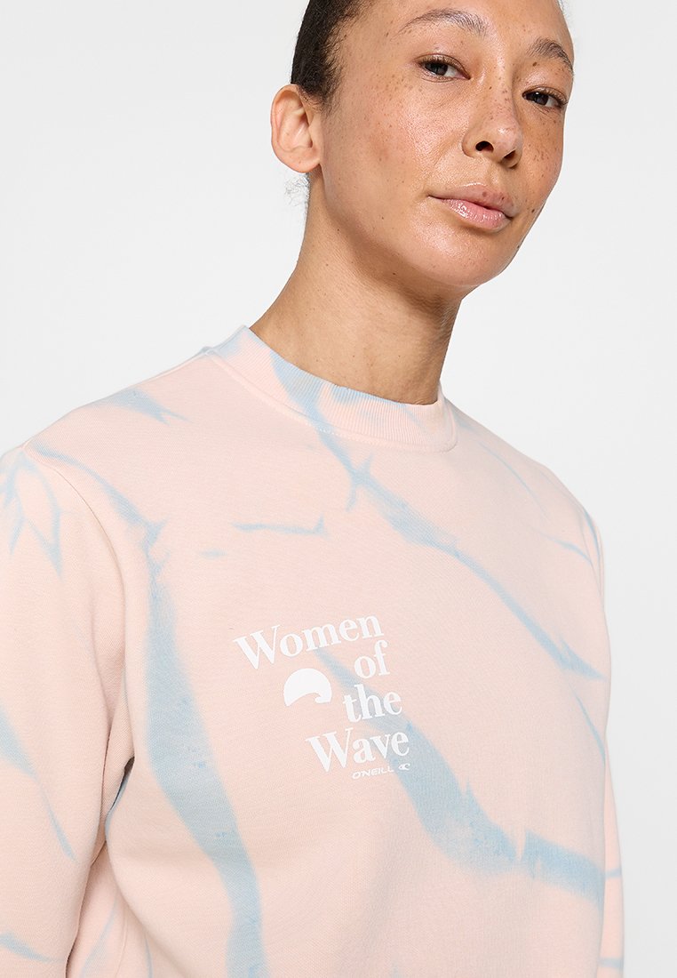 Helles rosa Sweatshirt mit blauen Batikmustern. Verfügt über einen Rundhalsausschnitt und weißen Drucktext "Women of the Wave" auf der Vorderseite.