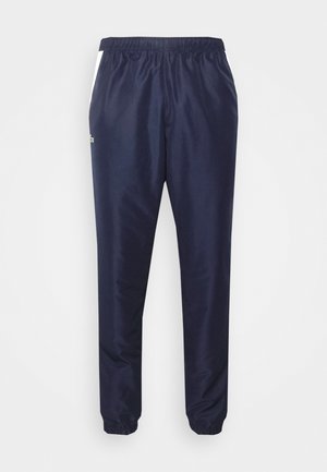 Pantalons de survêtement navy avec taille élastique, poignets fuselés et accents latéraux blancs. Fabriqués en tissu lisse et léger. Présente un détail logo.