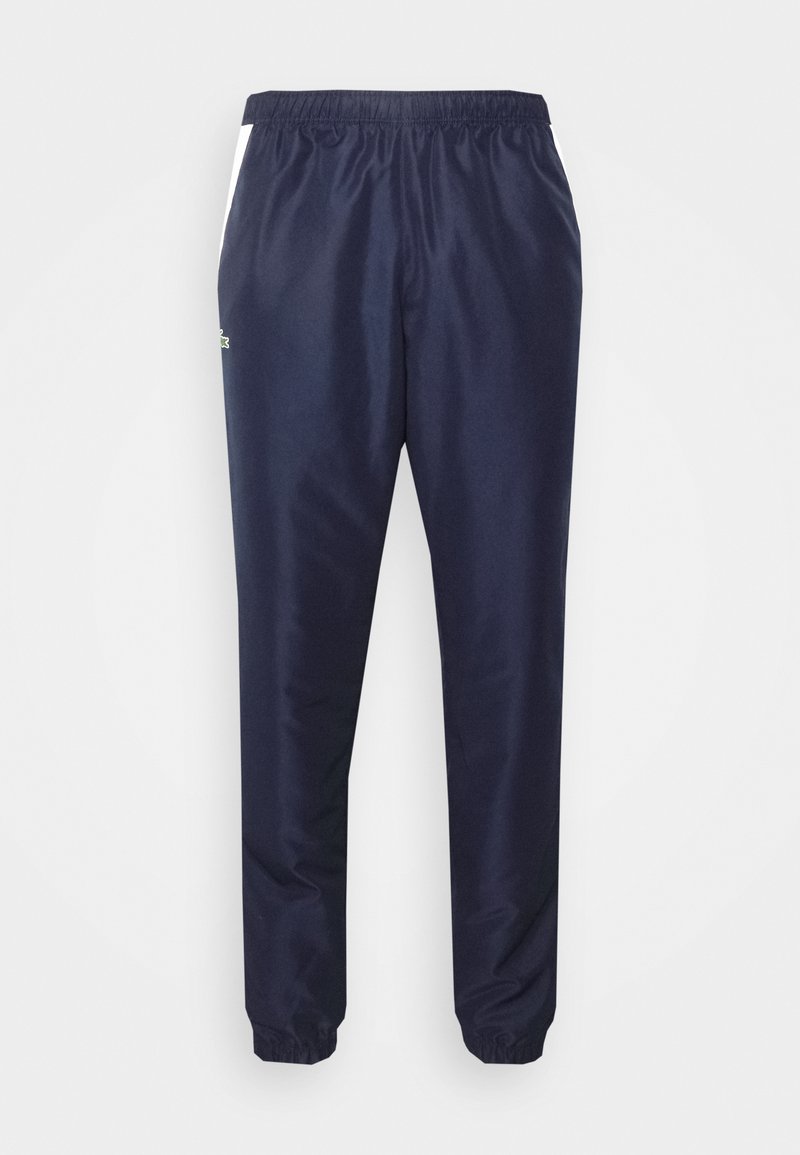 Pantalons de survêtement navy avec taille élastique, poignets fuselés et accents latéraux blancs. Fabriqués en tissu lisse et léger. Présente un détail logo.