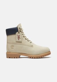 Beiger High-Top-Lederstiefel mit hellbrauner Gummisohle, navyfarbenem gepolstertem Kragen, beigen Schnürsenkeln und eingeprägtem Baum-Logo an der Ferse.